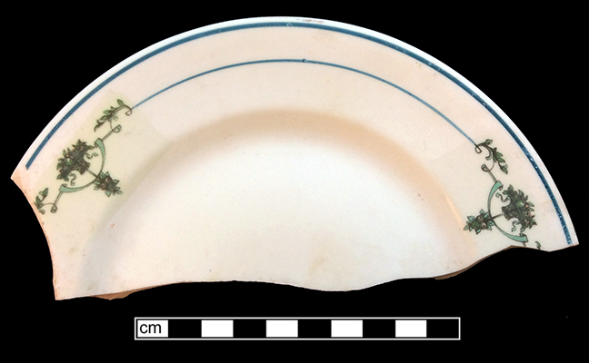 Plate, rolled rim. Unglazed bisque waster. Painted blue band and  line with floral decal. Note rectangular discoloration of residue from the decal application. Rim diameter: 7.25”. 2.5 mm thick.